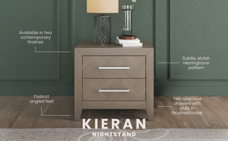 The Kieran Nightstand by Child Craft features a stylish herringbone pattern, angled feet, brushed nickel pulls, and two drawers in a Crescent Gray finish. A lamp and books rest on top, highlighting its modern design. "KIERAN NIGHTSTAND" appears below.