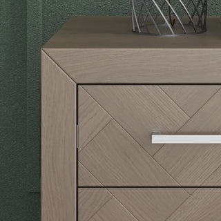Close-up of the Child Craft Kieran Nightstand in Crescent Gray, featuring a herringbone pattern, silver handle, and a metal wire decor piece on top, set against a textured green wall.