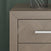 Close-up of the Child Craft Kieran Nightstand in Crescent Gray, featuring a herringbone pattern, silver handle, and a metal wire decor piece on top, set against a textured green wall.