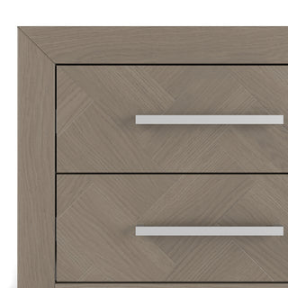 Close-up of the top corner of the Child Craft Kieran Nightstand in Crescent Gray, showing two drawers with long silver handles and a herringbone wood pattern in a light, natural finish.