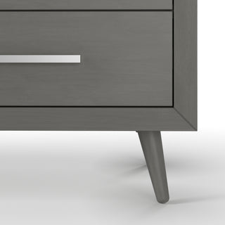 Close-up of the bottom corner of the Child Craft Cranbrook 4 Drawer Chest in Lunar Gray, featuring angled legs and a metallic horizontal drawer handle, set against a white background.