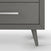 Close-up of the bottom corner of the Child Craft Cranbrook 4 Drawer Chest in Lunar Gray, featuring angled legs and a metallic horizontal drawer handle, set against a white background.