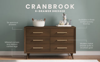 The Child Craft Cranbrook Double Dresser in Toasted Chestnut stands against a pale green wall, offering spacious drawers, mitered corners, brushed gold handles, and mid-century modern style—perfect nursery furniture.