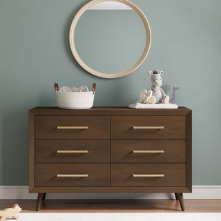 A Child Craft Cranbrook Double Dresser in Toasted Chestnut sits against a pale green wall. On top are a round mirror, basket, and plush zebra, elephant, and giraffe toys. A wooden toy on the floor completes this charming nursery scene.