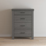 The Child Craft Denman 4 Drawer Chest in Midnight Gray stands against a light wall on a wood floor, offering stylish nursery storage with four drawers featuring black handles.