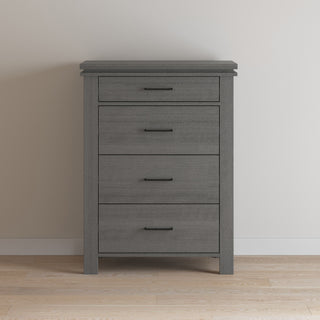 The Child Craft Denman 4 Drawer Chest in Midnight Gray stands against a light wall on a wood floor, offering stylish nursery storage with four drawers featuring black handles.