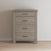 The Child Craft Denman 4 Drawer Chest in Crescent Gray, featuring sleek black handles, stands against a plain white wall on a light wood floor.