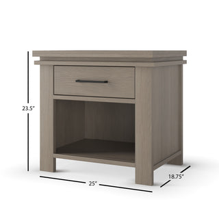 The Child Craft Denman Nightstand in Crescent Gray features a craftsman wood design with one drawer, a horizontal black handle, and an open shelf. Ideal for nurseries, it measures 23.5"H x 25"W x 18.75"D.