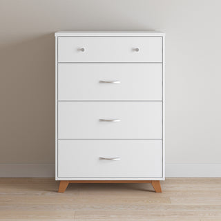 The Child Craft Soho 4 Drawer Chest in White/Natural features four drawers, wooden legs, and sleek silver handles, shown against a light wall on a wooden floor.