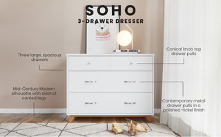 The Child Craft Soho 3-Drawer Dresser in White/Natural features spacious drawers, conical knobs, metal pulls, and a mid-century modern design with angled legs. A lamp and framed art are displayed on top against the wall.