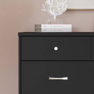 A Child Craft Soho 3-Drawer Dresser in Ebony stands against a light pink wall, topped with two stacked books and a white decorative coral sculpture.