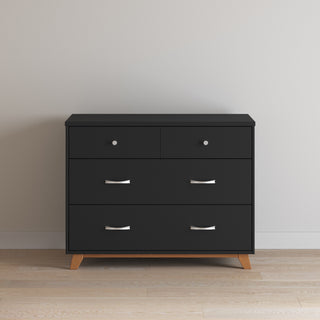 The Child Craft Soho 3-Drawer Dresser in Ebony, featuring a minimalist design with silver handles and short wooden legs, stands against a light wall on a wooden floor.