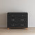 The Child Craft Soho 3-Drawer Dresser in Ebony, featuring a minimalist design with silver handles and short wooden legs, stands against a light wall on a wooden floor.