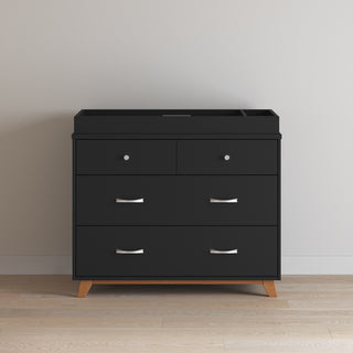 The Child Craft Soho 3-Drawer Dresser in Ebony features wooden legs, metal handles, and two small drawers above a large lower drawer, shown against a light wall and wood floor.