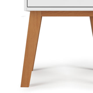 Close-up of the Soho Nightstand by Child Craft, featuring angled light brown legs and a white drawer in a mid-century modern style, set against a plain white background.