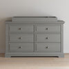 A Child Craft dresser featuring the F01792 Universal Changing Table Topper in Lunar Gray, six drawers with round knobs, rests against a plain white wall on a light wood floor.