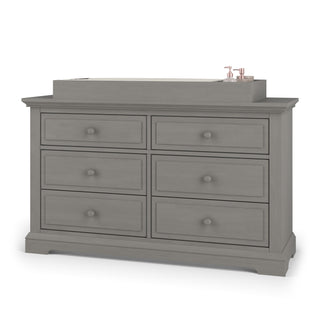 A Child Craft Universal Changing Table Topper in Lunar Gray (F01792) is shown on a dresser, with two small pink containers placed on the right.