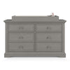 The Child Craft F01792 Universal Changing Table Topper in Lunar Gray sits atop a six-drawer dresser, displaying its ability to hold a changing mat and bottle. The scene is set against a white background.