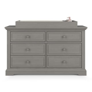 The Child Craft F01792 Universal Changing Table Topper in Lunar Gray sits atop a six-drawer dresser, displaying its ability to hold a changing mat and bottle. The scene is set against a white background.