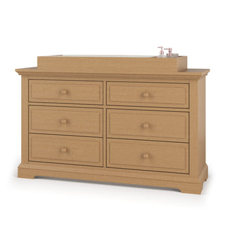 The Child Craft Legacy Changing Table Topper in Biscotti sits securely atop a wooden dresser with six drawers and round knobs, holding two pump bottles.