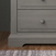 A close-up of the Child Craft Jordyn Nightstand in Lunar Gray shows its baby-safe finish, two drawers with round knobs, and carved base, standing on a wooden floor beside a patterned rug.