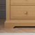 A close-up of the Child Craft Jordyn Nightstand, Ready-to-Assemble in Biscotti, displays two drawers with round knobs and crown molding. The nightstand is on a wooden floor, partly beside a dark gray wall.