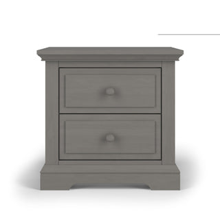 The Child Craft Jordyn Nightstand in Lunar Gray features two drawers with round knobs, a decorative crown-molded base with a recessed center, and baby-safe finishes. Ready-to-assemble for your convenience.