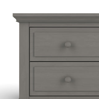 A close-up of the upper left corner of the Child Craft Jordyn Nightstand in Lunar Gray shows baby-safe finishes, classic lines, two drawers with round knobs, and subtle crown molding. Ready-to-assemble design.