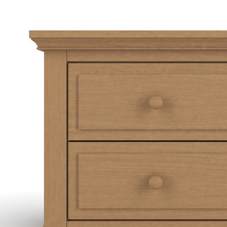 A close-up of the upper left corner of the Child Craft Jordyn Nightstand, Ready-to-Assemble in Biscotti finish, featuring two drawers with round wooden knobs and crown molding accents, shown against a white background.