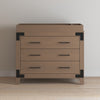 A wooden dresser with three drawers, black handles, and corner brackets is topped with the Child Craft F01792 Universal Changing Table Topper in Dusty Heather, creating a convenient baby changing station.