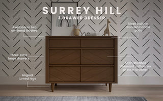 The Child Craft Surrey Hill 3 Drawer Dresser in Toasted Chestnut features three spacious drawers with diamond pattern fronts, angled legs, and built-in wooden handles, set against geometric wallpaper to showcase its stylish finishes.