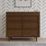 The Child Craft Surrey Hill 3 Drawer Dresser in Toasted Chestnut, featuring angled legs and geometric patterns, stands against a white wall with black diagonal lines. Framed art and decor items are arranged on top.