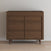 The Child Craft Surrey Hill 3 Drawer Dresser in Toasted Chestnut features angled legs and a geometric pattern on its drawer fronts, set against a plain white wall and a light wood floor.