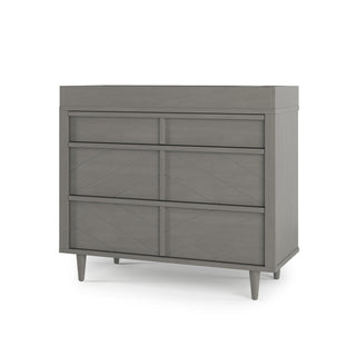 The Child Craft Surrey Hill 3 Drawer Dresser in Lunar Gray features three spacious drawers, a minimalist design, diamond-pattern detailing, and tapered legs, shown against a white background.