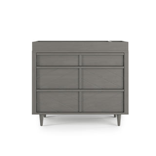 The Child Craft Surrey Hill 3 Drawer Dresser in Lunar Gray features simple geometric patterns and angled legs, presented against a plain white background.