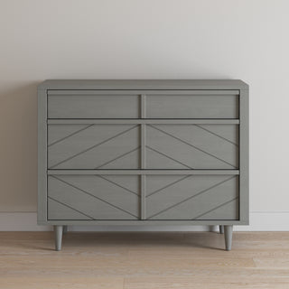 The Child Craft Surrey Hill 3 Drawer Dresser in Lunar Gray features a modern geometric pattern, making it a stylish addition to your nursery furniture collection, perfect against a white wall and light wooden floor.