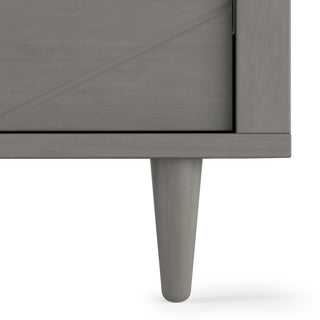 Close-up of the bottom corner of the Child Craft Surrey Hill 3 Drawer Dresser in Lunar Gray, showing its single tapered leg and door with subtle diagonal design—an ideal, stylish addition to any nursery.