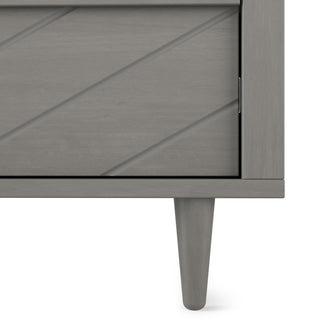 Close-up of the Child Craft Surrey Hill 5 Drawer Chest in Lunar Gray, featuring a gray finish, diagonal groove pattern on the door, and a single tapered leg visible at the bottom right.