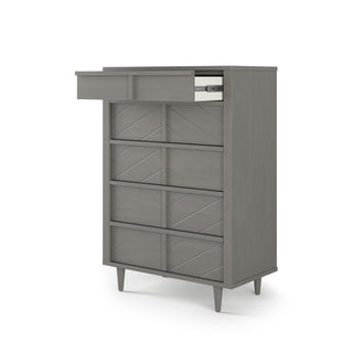 The Surrey Hill 5 Drawer Chest by Child Craft features a lunar gray finish, chevron front pattern, four tapered legs, and five drawers—one open to reveal neatly folded white and gray clothes—against a plain white background.