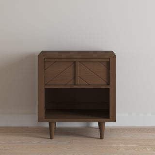 The Child Craft Surrey Hill Nightstand in Toasted Chestnut features a modern design with a single geometric-pattern drawer, open lower shelf, and four angled legs, shown against a plain light wall on a wooden floor.