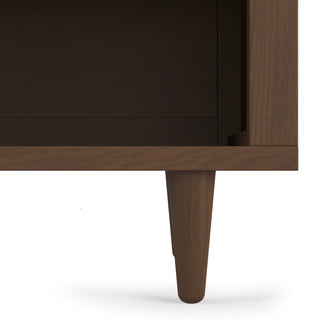 Close-up of the lower corner of the Child Craft Surrey Hill Nightstand in Toasted Chestnut, highlighting a single tapered leg and smooth brown finish with clean, modern lines.