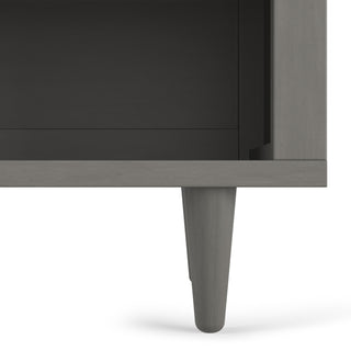 Close-up of the bottom corner of the Surrey Hill Nightstand by Child Craft in Lunar Gray, highlighting a tapered leg and part of an open shelf above.