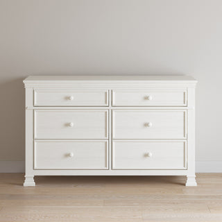 The Child Craft Westgate Double Dresser in Vintage Linen, featuring six drawers with round knobs, stands against a light beige wall on a pale wooden floor.