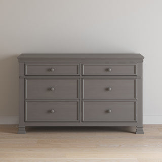 The Child Craft Westgate Double Dresser in Chelsea Gray, featuring six drawers with round knobs, is placed against a plain light wall on a light wood floor.