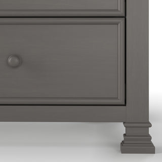 Close-up of the Westgate Double Dresser by Child Craft in Chelsea Gray, showing a round drawer knob, paneled drawer front, and carved square leg—perfect as a nursery dresser.