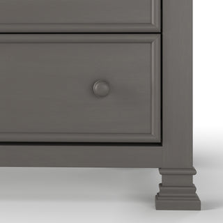 Close-up of the lower section of the Child Craft Westgate 5-Drawer Chest in Chelsea Gray, featuring one drawer with a round knob, decorative moldings, and part of its carved leg against a white background.
