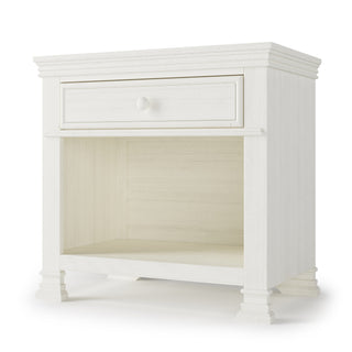 The Child Craft Westgate Nightstand in Vintage Linen is a white wooden nursery nightstand with one drawer, open lower shelf, decorative molding, and carved legs—ideal baby room furniture.