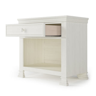 The Child Craft Westgate Nightstand in Vintage Linen is a classic white wood nightstand with one drawer, an open lower shelf, and four decorative legs—making it ideal furniture for your baby’s room.