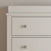 A close-up of the upper left corner of the Child Craft Harmony 3-Drawer Dresser with Changing Table Topper in Brushed Cotton shows two drawers with round metal knobs, set against a plain light-colored wall.