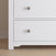 Close-up of the Child Craft Harmony 3-Drawer Dresser with Changing Table Topper in Matte White, featuring round silver knobs. Perfect for nursery storage, shown on a light wood floor beside a beige wall with white baseboards.